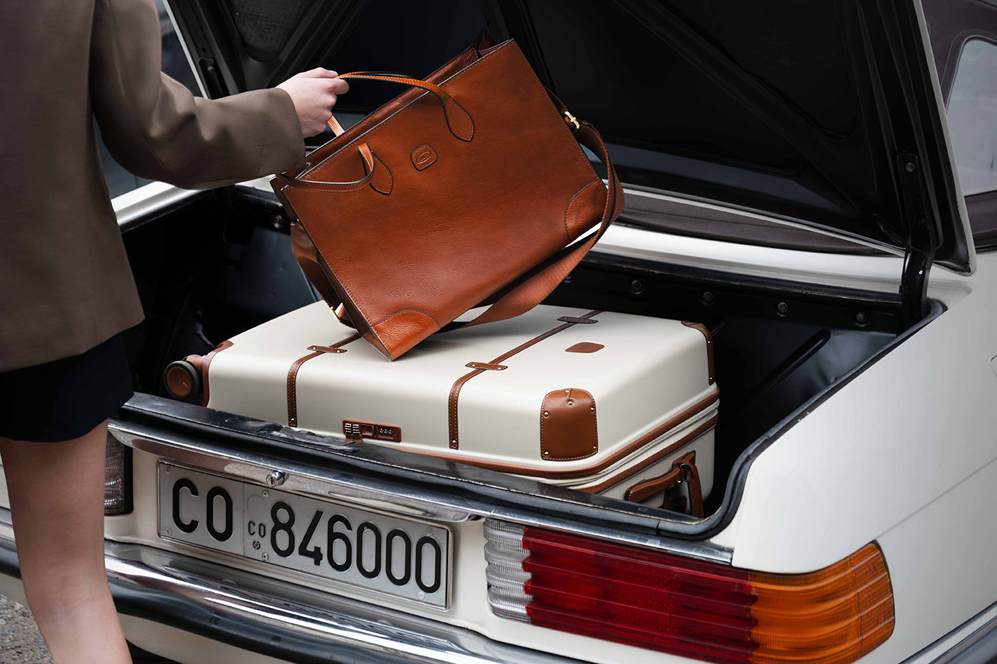 Woman loading premium leather Bric's luggage into car trunk