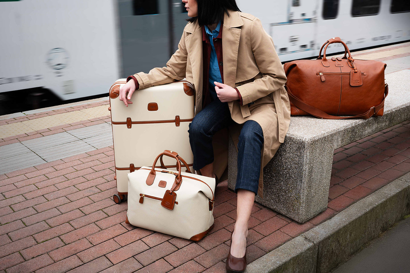 Woman sitting with durable hardside and leather luggage at a train station